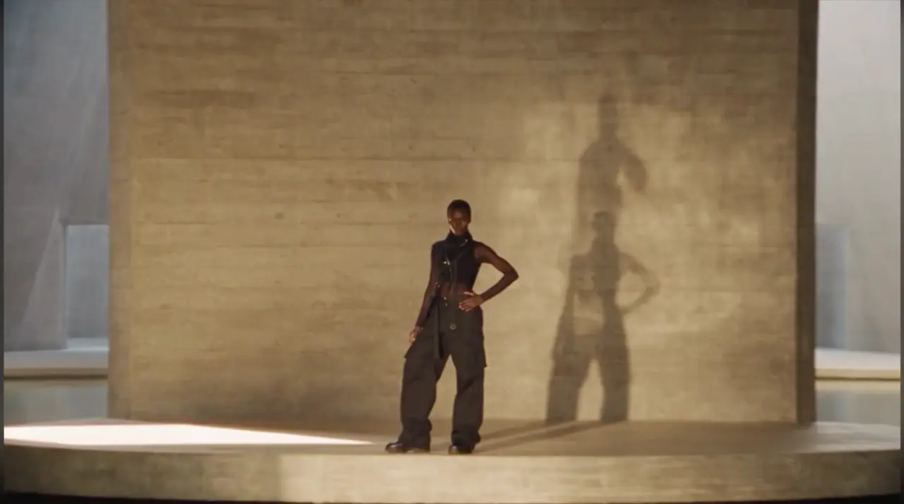 A model casts a sculptural shadow across a warm stone wall